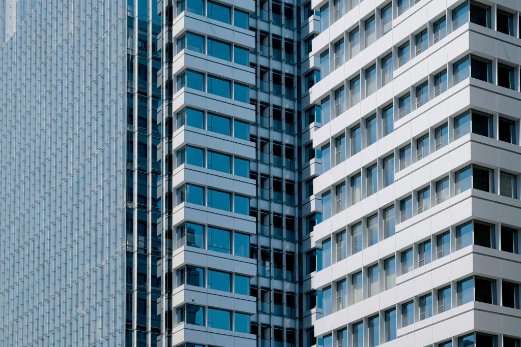Vista detallada de fachadas de edificios de oficinas modernos, con ventanales de vidrio y estructuras metálicas en tonos gris y blanco.